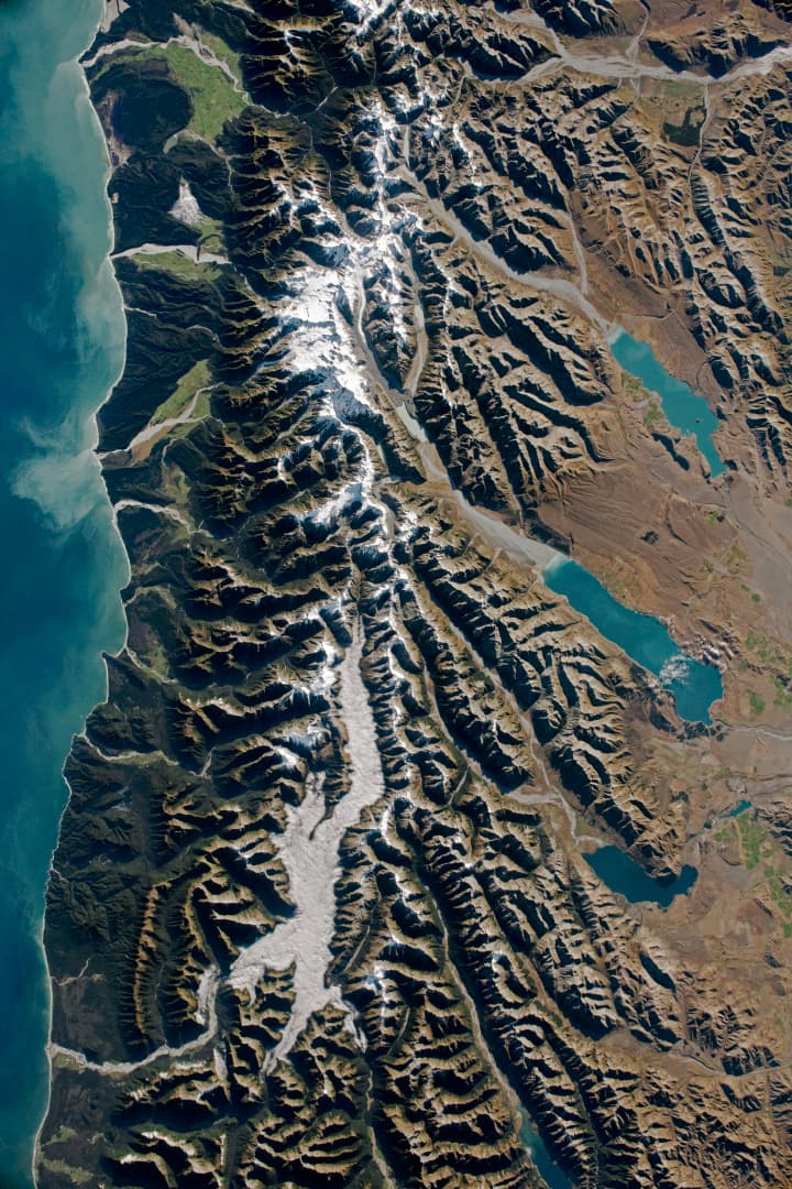 Astronaut photograph of New Zealand's Southern Alps, braided rivers, glacial valleys, and turquoise lakes.